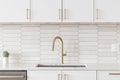 A kitchen faucet detail with a gold faucet, brown backsplash, and white cabinets. Royalty Free Stock Photo