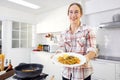 In the kitchen at home, a beautiful woman with a tablet prepares a pasta meal, and a lovely young woman eats pasta