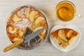 Knife on apple pie in mold, cup of tea with lemon, slice of charlotte in saucer on wooden table. Top view Royalty Free Stock Photo