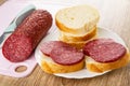 Knife, piece of sausage on cutting board, slices of bread, sandwiches with sausage in plate on wooden table Royalty Free Stock Photo