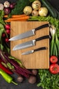 Kitchen Knives on Wooden Chopping Board with Fresh Vegetables Background. Vegetarian Raw Food. Royalty Free Stock Photo