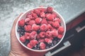 In the kitchen, a man's hand holds a bowl full of frozen raspberries. Frozen Summer Berries in a Bowl - Tasty Royalty Free Stock Photo