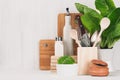 Kitchen modern decor - beige wooden utensils, brown cutting boards, green plant on soft light white wood background.