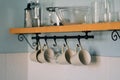 Kitchen open wooden shelf with dishes, glasses and mugs. Mugs are hanging from hooks. Cozy interior in a country house. Royalty Free Stock Photo