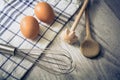 Kitchen Setting With 2 Eggs, Towel, Wooden Spoon And Querl And An Eggbeater On A Table