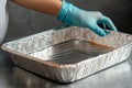 In a kitchen setting, food is being placed hand in glove into an aluminum container during preparation Royalty Free Stock Photo