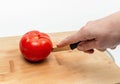 Cutting red tomato with knife into two halves on wooden kitchen board. Woman's hand cuts a tomato