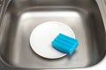 Kitchen sink with clean white plate and blue cleaning sponge Royalty Free Stock Photo