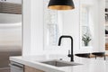 A kitchen sink detail with a black faucet and a black and gold pendant light. Royalty Free Stock Photo