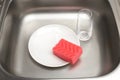 Kitchen sink with plate, pink cleaning sponge and drinking glass Royalty Free Stock Photo