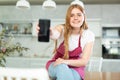 in kitchen,smiling red-haired girl in polka-dot apron shows blank smartphone screen close-up