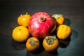 Kitchen still-life. Wholesome ripe fruits of pomegranate, mandarine and persimmon on a dark brown table. Royalty Free Stock Photo