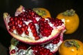 Kitchen still-life. Wholesome ripe fruits of pomegranate and persimmon on a dark brown table. Royalty Free Stock Photo