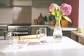 On the kitchen table is a rolling pin, there is a transparent glass bowl and a glass, next to a bouquet of hydrangeas