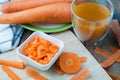 kitchen table with slice fresh carrot on cutting board and orange juice on glass of water.