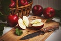 On the kitchen table still life - wicker basket with red ripe apples, next to it a wooden board on which lies an apple cut in Royalty Free Stock Photo