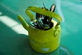 Kitchen utensils and cutlery in old fashioned green vintage teapot in bucket on table along with pepper shaker. Vintage Whistling