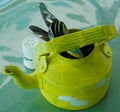 Kitchen utensils and cutlery in old fashioned green vintage teapot in bucket on table along with pepper shaker. Vintage Whistling