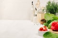 Kitchen white interior with raw fresh green salad, red cherry tomatoes, kitchenware on soft white wood table, copy space.