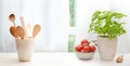 Kitchen window sill decorated with a potted basil plant, wooden cooking spoons, bowl with tomatoes and an onion against white Royalty Free Stock Photo