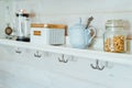 Kitchen wooden shelf with tea leaves in gold box and accessories, blue sugar bowl with spoon, strainer, press. Cup, mug hooks. Royalty Free Stock Photo