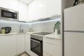 Kitchenette with plain white cabinets and chest of drawers, matching stone countertops and built-in appliances and white fridge