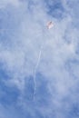 Kite flying high up in blue sky with long white streamer trailling below it Royalty Free Stock Photo