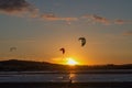 Kite surfers at sunset against a flaming orange sky.