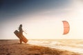 Kiteboarding. Kitesurfing athlete woman at sunset stands on the sandy shore holding her kite in the air and looks at the