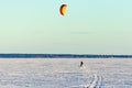 A kiter on skis under a colored dome rides on the big Onega Lake on a hard snow crust.