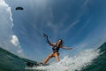 Kitesurfing girl in black sexy swimsuit with kite in sky on board in blue sea riding waves with water splash. Royalty Free Stock Photo