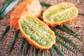 Kiwano or african horned melon with palm leaves on rattan background. Cutted hedged gourd, african horned cucumber, english tomato