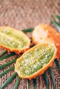 Kiwano or african horned melon with palm leaves on rattan background. Cutted hedged gourd, african horned cucumber, english tomato