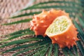 Kiwano or african horned melon with palm leaves on rattan background. Cutted hedged gourd, african horned cucumber, english tomato