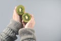 Kiwi fruit, half cut 2 pieces on women hands with sweater on light grey background.horizontal image