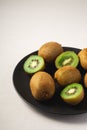 Kiwi fruits half sliced in black plate on vibrant plain white background Royalty Free Stock Photo