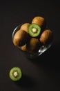 Kiwi fruits half sliced in glass bowl on dark black moody plain background