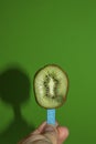 kiwi on a wooden stick, summer composition fruit ice cream in hand creative concept on a spring green background Royalty Free Stock Photo