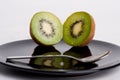 Kiwis next to each other on a black plate in front of a teaspoon Royalty Free Stock Photo