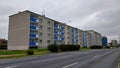 Four story gray block of flats with blue balconies standing by the empty wide road during cloudy weather