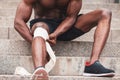 Knee injury concept, afro american guy bandaging his leg with a bandage, a man injured his knee in training