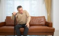 senior guy sits on a sofa with a walking stick in his living room at home Royalty Free Stock Photo