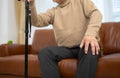 senior guy sits on a sofa with a walking stick in his living room at home Royalty Free Stock Photo