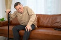 senior guy sits on a sofa with a walking stick in his living room at home Royalty Free Stock Photo