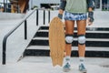 Knee-padded legs of a woman skater holding a board at skatepark