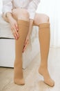 Knee socks or socks. Beige compression stockings on a woman in a white room. Girl putting on stockings at home Royalty Free Stock Photo