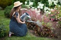 A young girl kneels down and waters the flowers in her garden with a watering can.