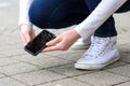 Kneeling person picking up broken phone on street