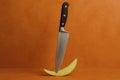 Knife balancing on a green apple slice against an orange backdrop in a kitchen setting Royalty Free Stock Photo