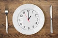 Knife, fork, white plate with clock showing lunch time on old wood table Royalty Free Stock Photo